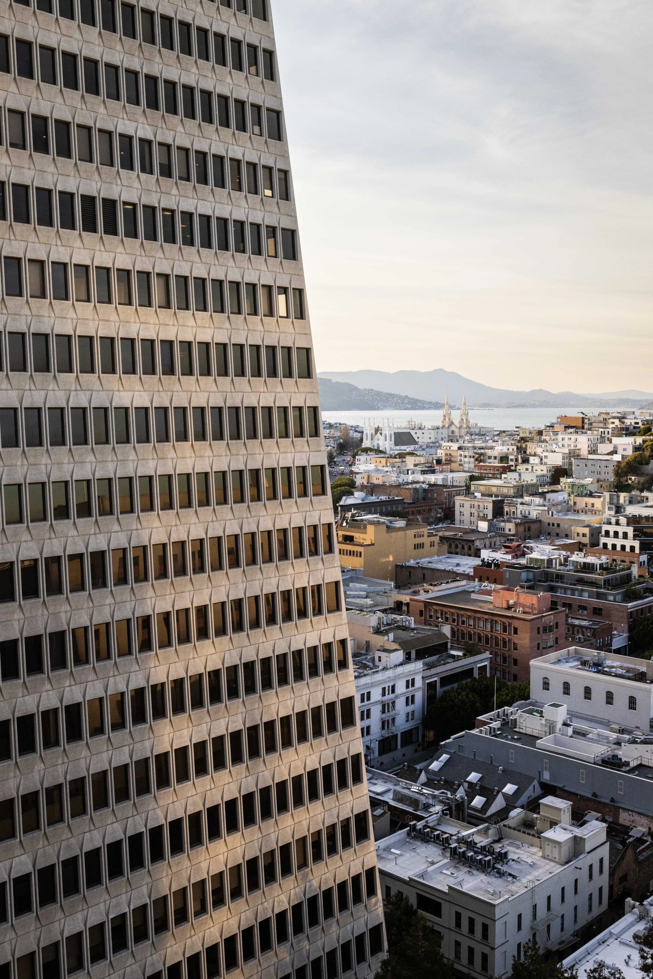 The Transamerica Pyramid’s windowed facade beside San Francisco rooftops and the bay.